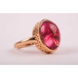 A yellow metal and tourmaline ring set with an oval cabochon pink tourmaline, measuring