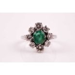 An emerald and diamond cluster ring, the oval cut emerald in four claw mount within a border of
