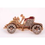 An unsual yellow metal and paste stone brooch in the form of a vintage car, with moving wheels,