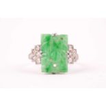 An early 20th century 18ct white gold, diamond, and jade ring, set with a pierced and carved