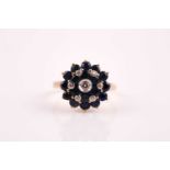 A yellow metal, diamond, and sapphire roundel cluster ring, centred with a collet-set diamond,