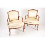 A pair of French Louis XV carved beechwood fauteuils with ivory satin stuff over the upholstery, the