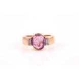 A yellow metal, diamond, and sapphire ring, set with a mixed oval-cut purplish pink sapphire, of