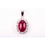 A silver, ruby, and white sapphire pendant of oval design, set with a cabochon glass-filled ruby,