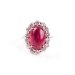 A silver, cubic zirconia, and glass-filled ruby cocktail ring, set with a bright red oval cabochon