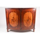 A George III satinwood crossbanded mahogany bowfront two-door drawing room cabinet, the shaped doors