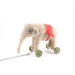An early 20th century possibly Steiff blonde plush pull along elephant. With red felt howdah,