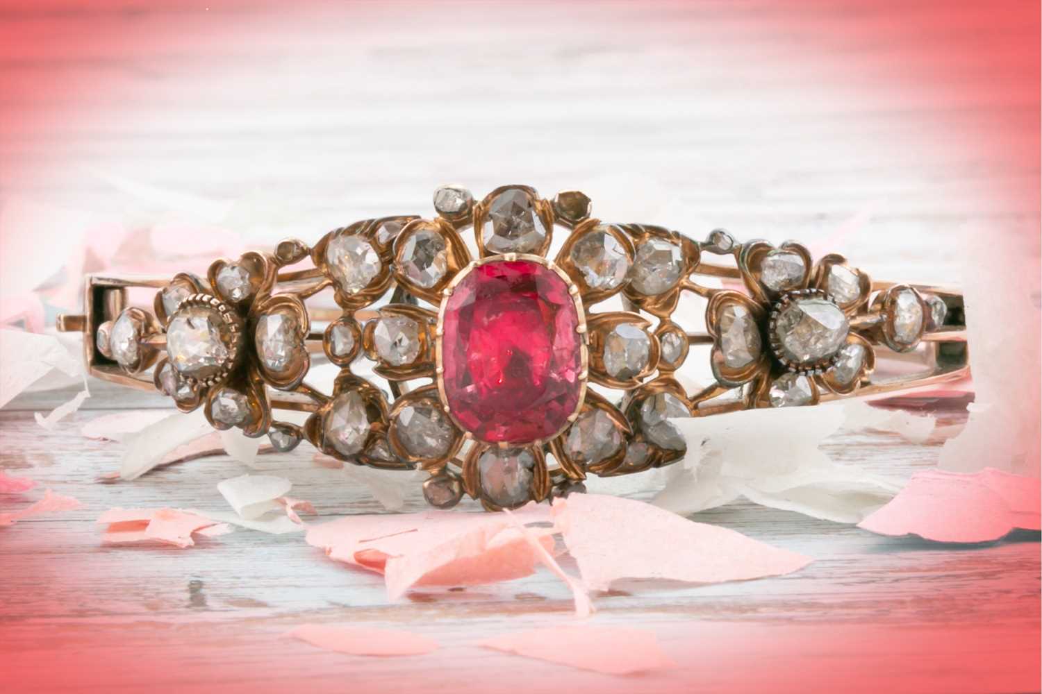 An antique yellow metal and diamond bangle, set with a reddish pink central stone, likely spinel,