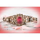 An antique yellow metal and diamond bangle, set with a reddish pink central stone, likely spinel,