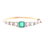 A Victorian yellow gold, diamond, and emerald bangle, centred with a mixed square-cut emerald,