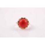 A Continental yellow metal and coral ring, set with a round cabochon coral within a shaped gold
