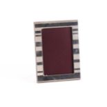 Cartier. A silver photograph frame; rounded rectangular with horizontally banded decoration.