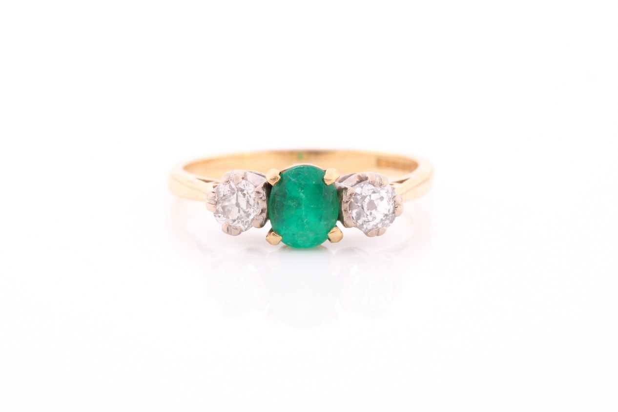 A three stone half hoop emerald and diamond ring. The oval cut emerald in four claw mount flanked by