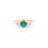 A three stone half hoop emerald and diamond ring. The oval cut emerald in four claw mount flanked by