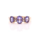 A yellow metal and tanzanite ring, set with three mixed oval-cut tanzanites, interspersed with