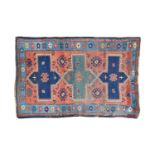 An old red gound Kazak rug. With three hooked conjoined lozenges on a field of sand spiders.