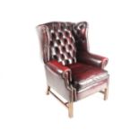A George III style deep button "Ox Blood" hide upholstered hipped wing back fireside chair. With