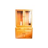 An Ercol golden dawn light elm two-section display cupboard. With two glazed doors above a base with