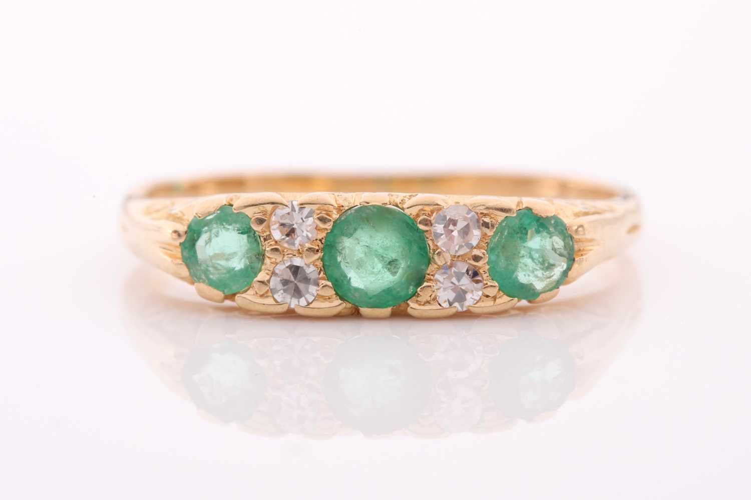 An early 20th century gold, emerald and diamond carved half-hoop ring, the three slightly