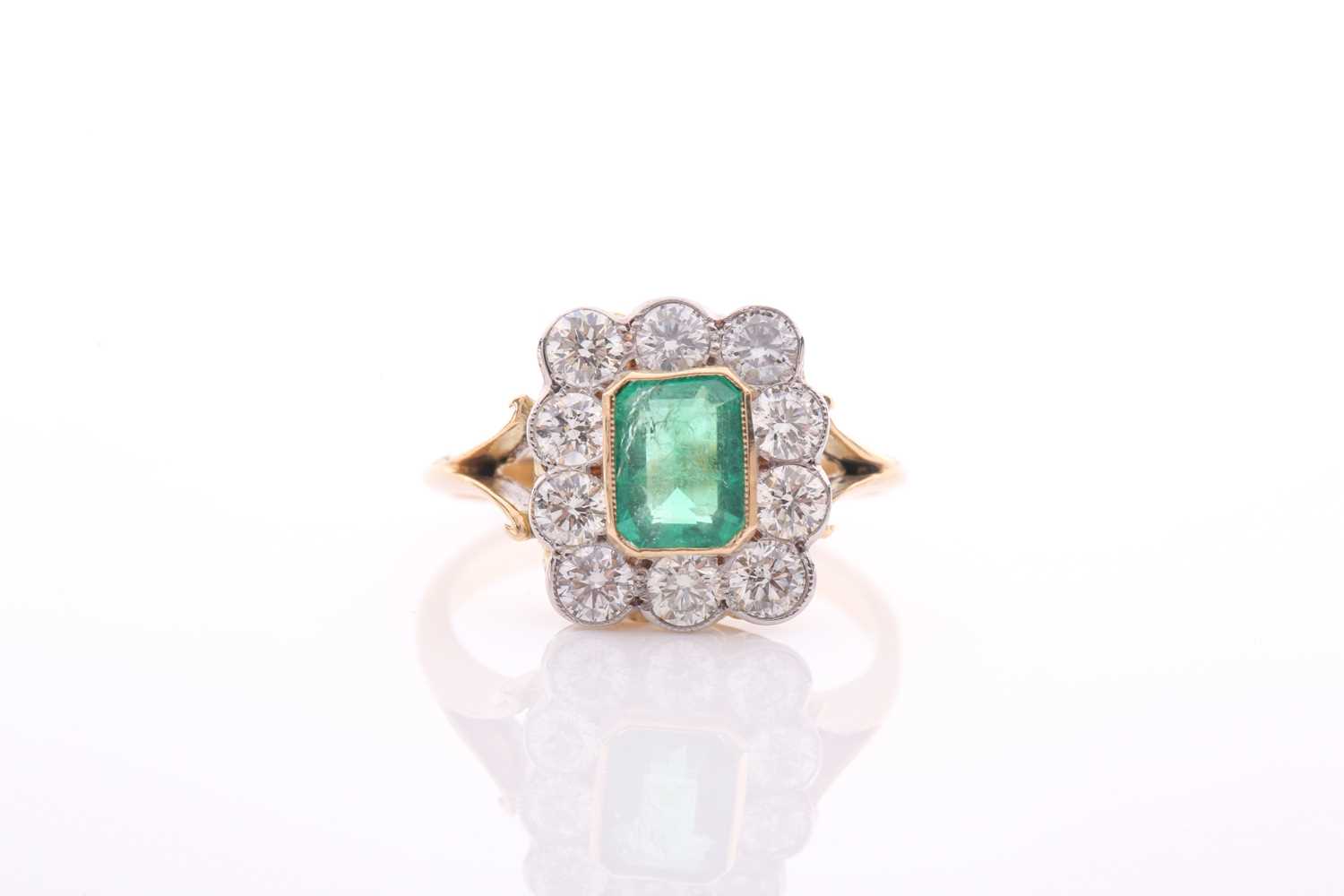An emerald and diamond rectangular cluster ring, centred with an emerald-cut emerald,