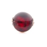 A yellow metal and amber ring, set with a round cabochon cherry-coloured piece of amber, in a