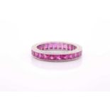 A ruby eternity ring, set with mixed faceted rubies, in a white metal mount with engraved decoration