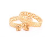 A pair of Indian yellow metal bracelet bangles, with bright-cut openwork design, each suspended with