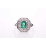 A platinum, diamond, and emerald ring, set with an emerald-cut emerald within a chamfered border