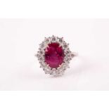 A ruby and diamond cluster ring; the oval brilliant step cut ruby in four claw mount within a border