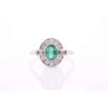 A platinum, diamond, and emerald dress ring, set with a mixed oval-cut emerald, within a border of