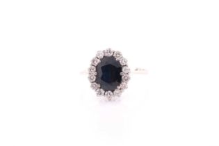 A white metal and sapphire cluster ring, set with a mixed oval-cut dark blue sapphire within a