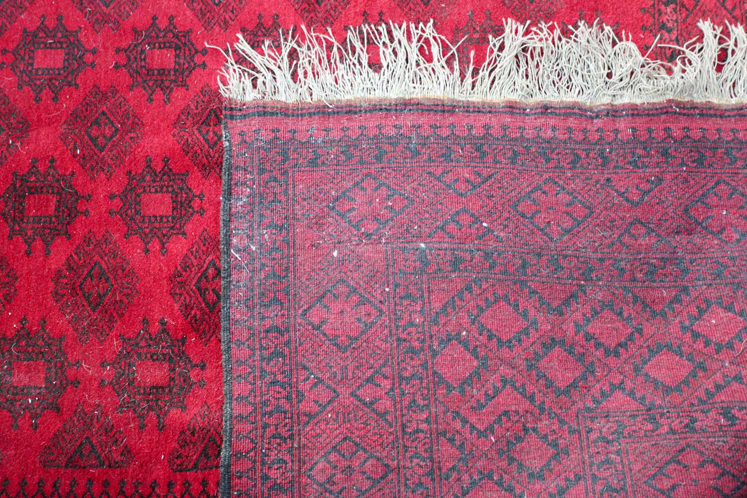 A 20th-century madder red ground Afghan carpet, with an open field of multi-point star-shaped - Image 4 of 4