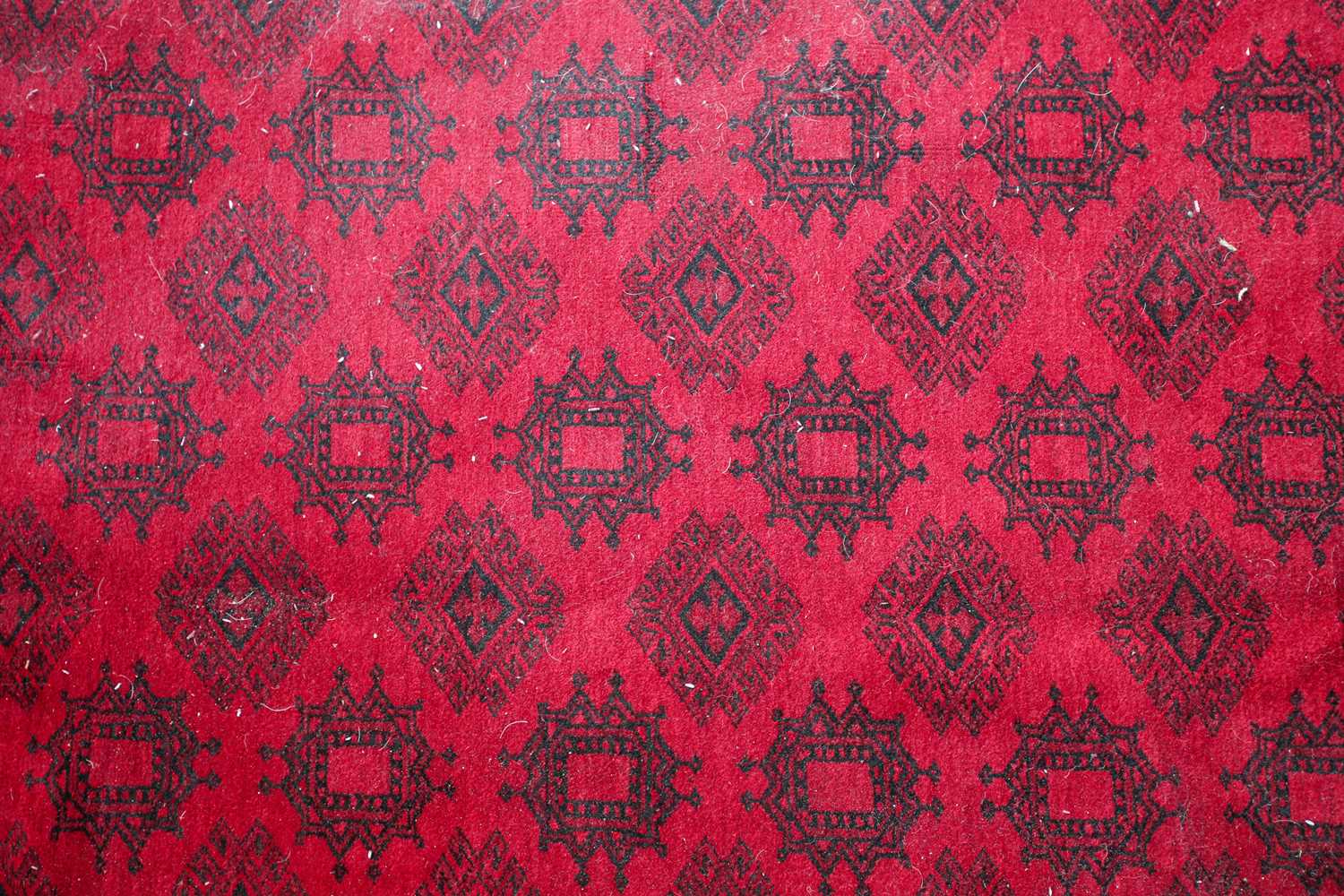 A 20th-century madder red ground Afghan carpet, with an open field of multi-point star-shaped - Image 2 of 4