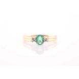 A modern 18ct gold, emerald and diamond three stone ring, centred with an oval mixed-cut emerald