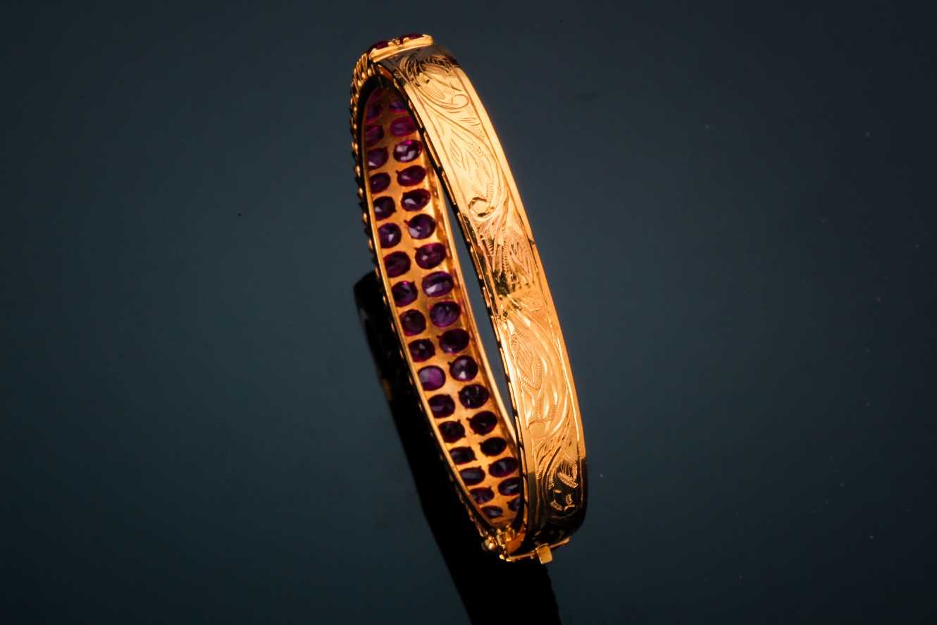 A ruby bangle; composed of two rows of mixed oval cut rubies in carved claw mounts to a foliate - Image 2 of 4