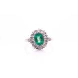 A platinum, diamond, and emerald cluster ring, set with a mixed oval-cut emerald of approximately