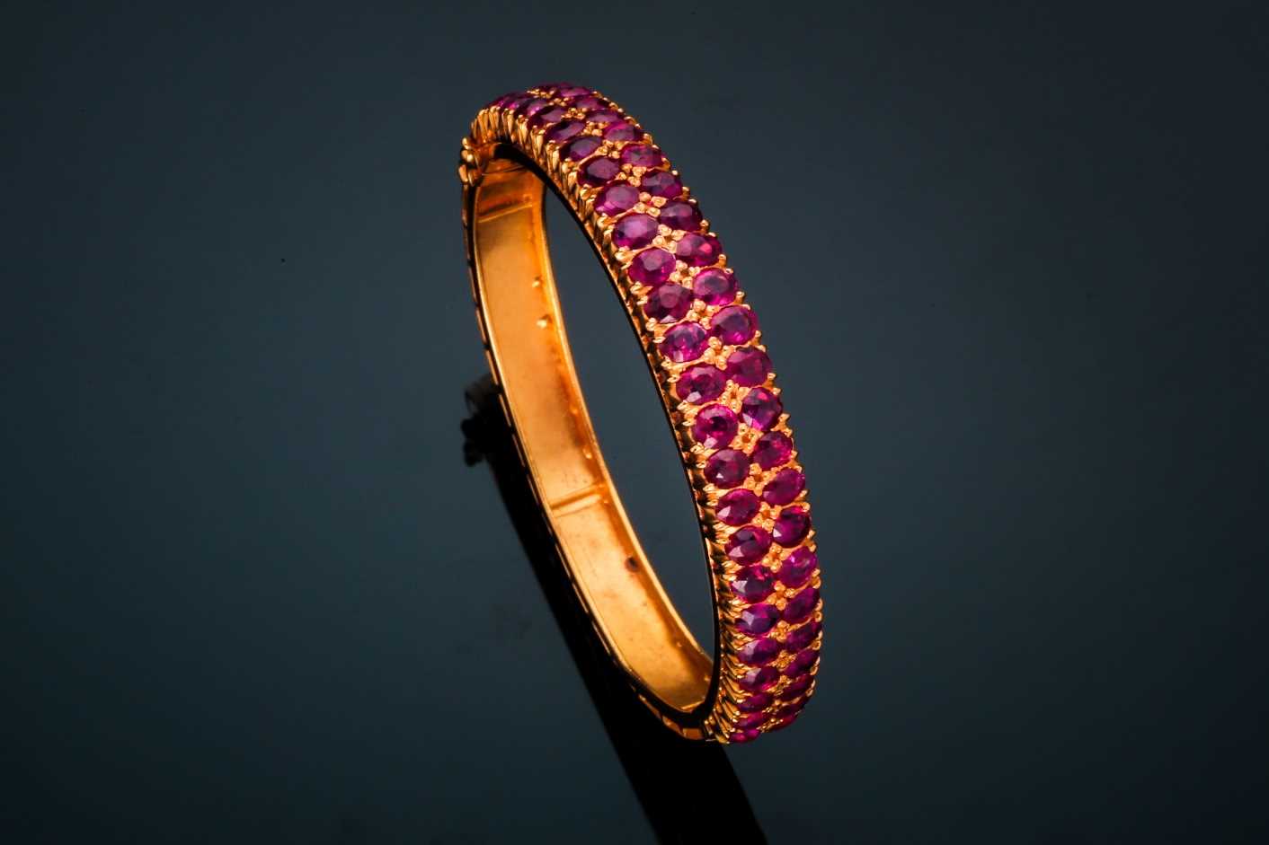 A ruby bangle; composed of two rows of mixed oval cut rubies in carved claw mounts to a foliate