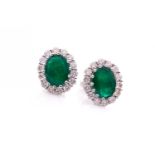 A pair of diamond and emerald cluster earrings, each set with a mixed oval-cut emerald, within a