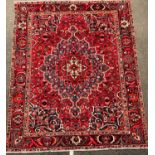 A large red ground Heriz style Baktiari carpet with central star form medalion within broad leafy