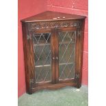An oak Jaycee floor standing corner cupboard, canted front, demi-lune carving to frieze, two lead