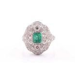 An Art Deco style diamond and emerald ring; the central emerald cut emerald in millegrain mount