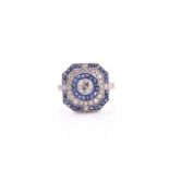 A platinum, diamond, and sapphire cluster ring, centred with a round-cut diamond within a