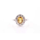 A diamond and yellow sapphire cluster ring, set with a mixed oval-cut sapphire, within a border of