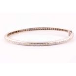 A diamond bangle; set with a line of round brilliant cut diamonds along a curved and polished