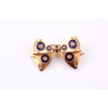 An 18ct yellow gold bow brooch, designed with cobalt blue enamel circular patterns, 3.8 cm wide, 6.1