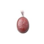 A probably Middle Eastern oval white metal pendant inset with an agate panel carved with a seated
