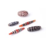A collection of five Tibetan carved agate Dzi beads of turned elliptical form, some with banded