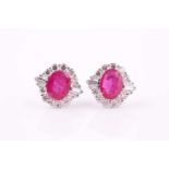 A pair of ruby and diamond earrings, each centred by a 9 x 7mm round cut pinkish-purple ruby, within