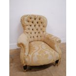 A 19th century button backed arm chair upholstered in yellow floral fabric, raised on brass