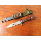 A WOODEN HANDLED MILITARY BAYONET, with serrated blade, a metal scabbard stamped SV132, and a
